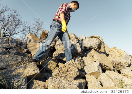 a man works with a pile of stones and broken pieces of concrete, carries construction debris a man works with a pile of stones and broken pieces of concrete, carries construction debris 83426575