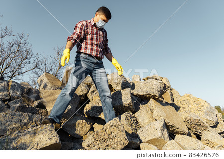 a man works with a pile of stones and broken pieces of concrete, carries construction debris a man works with a pile of stones and broken pieces of concrete, carries construction debris 83426576