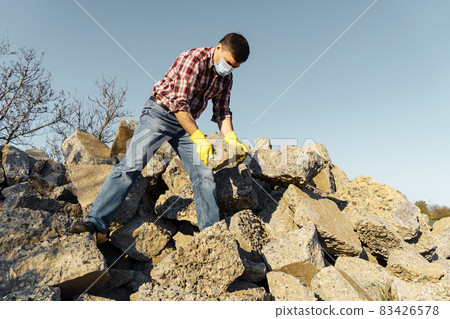 a man works with a pile of stones and broken pieces of concrete, carries construction debris a man works with a pile of stones and broken pieces of concrete, carries construction debris 83426578