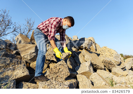 a man works with a pile of stones and broken pieces of concrete, carries construction debris a man works with a pile of stones and broken pieces of concrete, carries construction debris 83426579