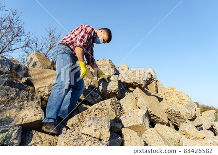 a man works with a pile of stones and broken pieces of concrete, carries construction debris a man works with a pile of stones and broken pieces of concrete, carries construction debris 83426582