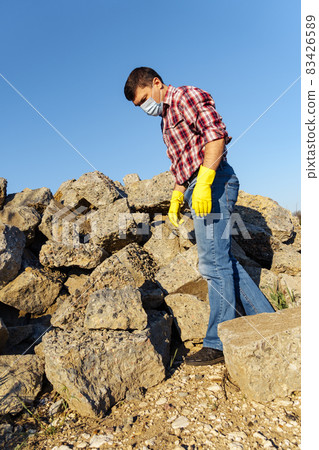 a man works with a pile of stones and broken pieces of concrete, carries construction debris 83426589