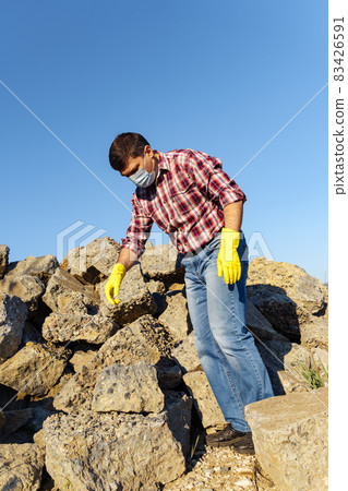 a man works with a pile of stones and broken pieces of concrete, carries construction debris a man works with a pile of stones and broken pieces of concrete, carries construction debris 83426591