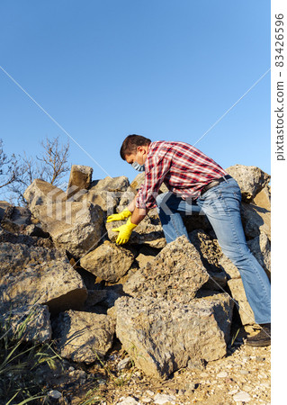 a man works with a pile of stones and broken pieces of concrete, carries construction debris a man works with a pile of stones and broken pieces of concrete, carries construction debris 83426596