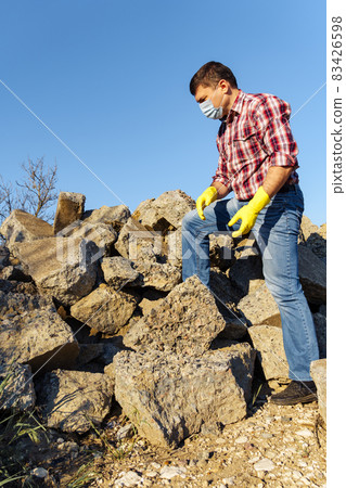 a man works with a pile of stones and broken pieces of concrete, carries construction debris a man works with a pile of stones and broken pieces of concrete, carries construction debris 83426598