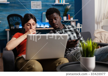 Modern interracial couple with pregnancy sitting on sofa 83428977