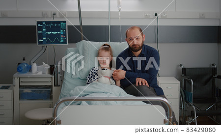 Portrait of sad father holding sick child hands looking into camera during medical consultation Portrait of sad father holding sick child hands looking into camera during medical consultation 83429080