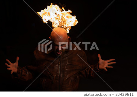 Bald man in a leather jacket with a burning head on a dark background. Bald man in a leather jacket with a burning head on a dark background. 83429611