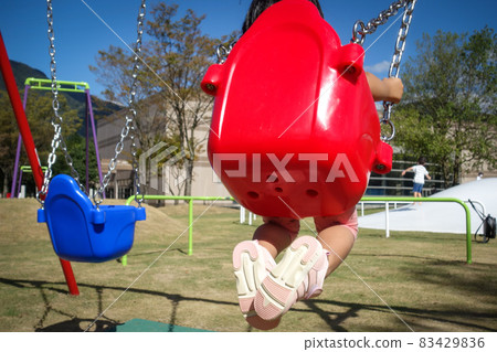 Kids playing on a swing for toddlers in the park Kids playing on a swing for toddlers in the park 83429836