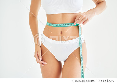 Young slim woman measuring her waist by measure tape on white background Young slim woman measuring her waist by measure tape on white background 83431229