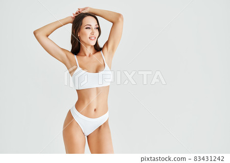 Smiling sporty woman in white underwear posing on studio background with copy space Smiling sporty woman in white underwear posing on studio background with copy space 83431242