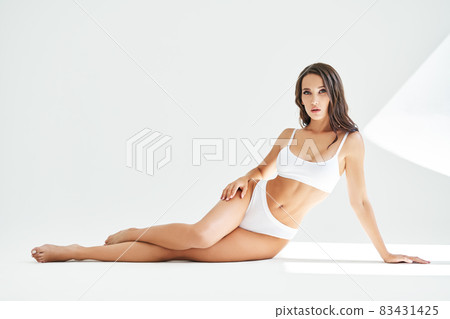 Young beautiful woman with perfect body in underwear sitting on floor posing on studio 83431425