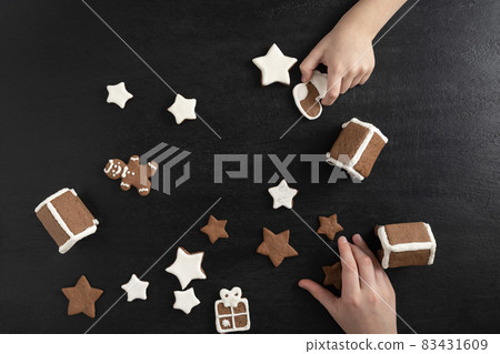 Children are getting ready for Christmas. Sugar glazed gingerbread cookies in children's hands. Black background Children are getting ready for Christmas. Sugar glazed gingerbread cookies in children's hands. Black background 83431609