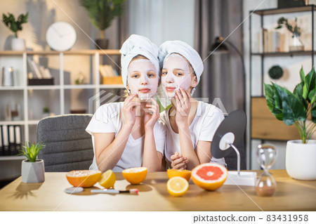 Two sisters posing at home with hydration sheet mask on face Two sisters posing at home with hydration sheet mask on face 83431958