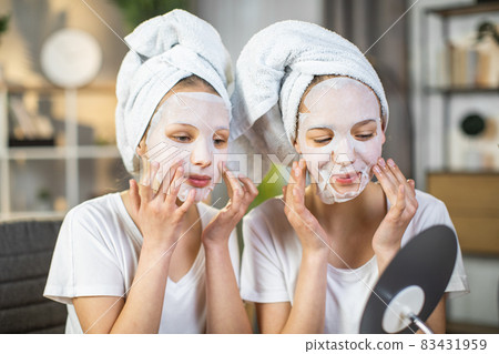 Two female teenagers using cosmetic mask for face and looking in the mirror 83431959
