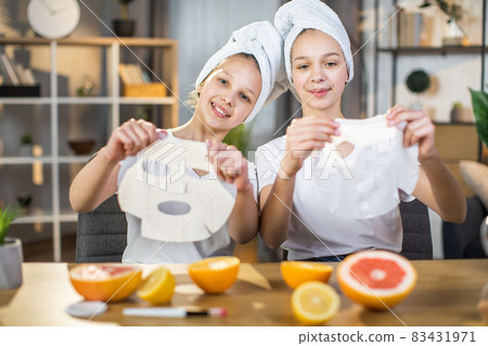 Two sisters holding vitamin mask for face at desk Two sisters holding vitamin mask for face at desk 83431971