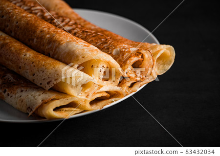 Thin pancakes on a plate on a black background. Traditional Russian food. Thin pancakes on a plate on a black background. Traditional Russian food. 83432034