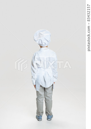 Back view of little boy in white cook uniform and huge chef's hat standing isolated on white studio background. Back view of little boy in white cook uniform and huge chef's hat standing isolated on white studio background. 83432157