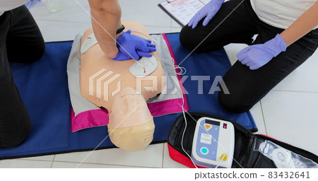 CPR training medical procedure workshop. Demonstrating chest compressions and use of AED automatic defibrillator on CPR doll 83432641