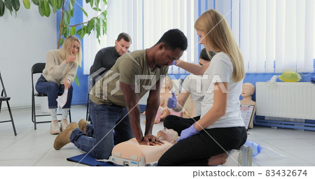 Young woman instructor showing how to make chest compressions with dummy during the first aid group training indoors. 83432674