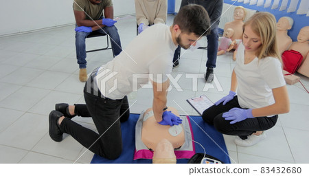 CPR training medical procedure workshop. Demonstrating chest compressions and use of AED automatic defibrillator on CPR doll. 83432680