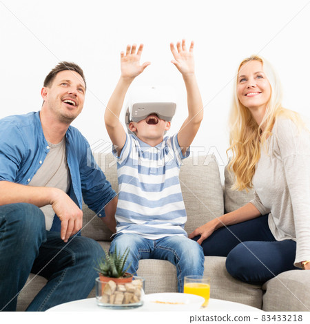 Happy family at home on living room sofa having fun playing games using virtual reality headset 83433218