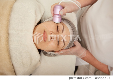 Smiling woman receiving facial treatment in cosmetology clinic 83434507