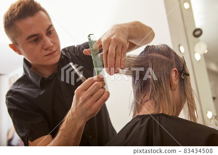 Handsome hairdresser cutting woman hair with professional scissors 83434508