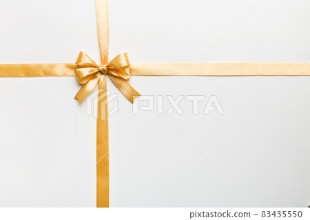 Top view of gold ribbon rolled and yellowbow isolated on colored background. Flat lay with copy space 83435550