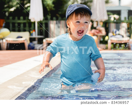 Cute toddler bathing in swimming pool. Little boy in bright blue swimwear playing in paddling pool. Vacation in hotel. Beach accessories. Cute toddler bathing in swimming pool. Little boy in bright blue swimwear playing in paddling pool. Vacation in hotel. Beach accessories. 83436957