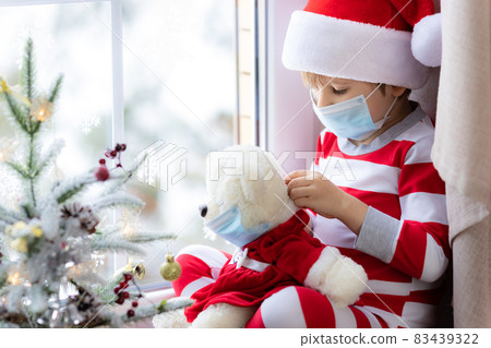 Happy child wearing Christmas pajamas sitting on windowsill 83439322