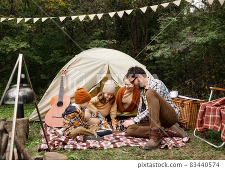 Happy smiling family playing chess game at campsite during camping trip in nature Happy smiling family playing chess game at campsite during camping trip in nature 83440574