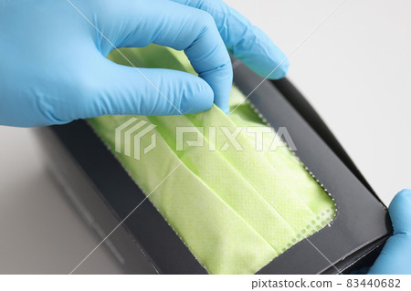 Rubber gloved hand pulling protective medical face mask out of box closeup Rubber gloved hand pulling protective medical face mask out of box closeup 83440682