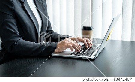 Business woman in suit is searching investment data of business and typing summary report on laptop while sitting 83441497
