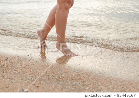 tanned legs in the sand close-up. a wave rolls onto the sand. summer vacation by the sea tanned legs in the sand close-up. a wave rolls onto the sand. summer vacation by the sea 83449167
