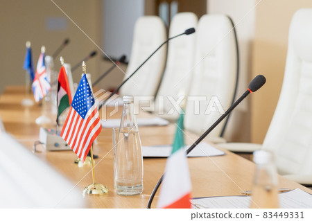 National flags placed on wooden conference table with microphones, papers and bottles of water 83449331