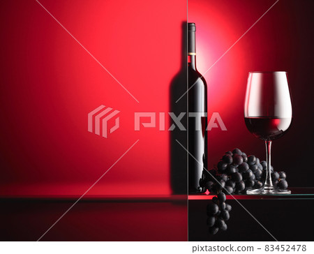 Bottle and a glass of red wine with a bunch of blue grapes. 83452478