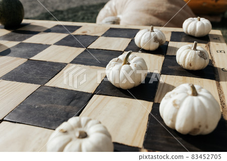Small white Halloween pumpkins as garden decoration on a classic wood chess or checkers board. Halloween and Thanksgiving natural DIY ideas for home and celebration concept. Close up, copy space 83452705
