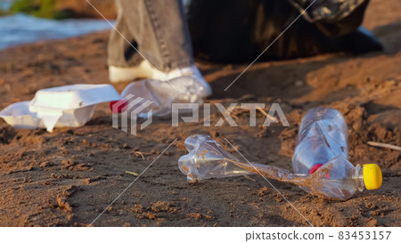 Unrecognizable woman in gloves collects plastic bottles in a black package near the river 83453157