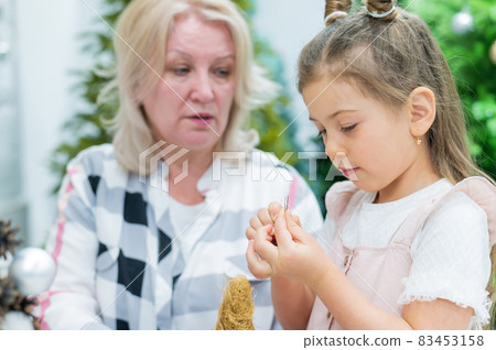 Elderly caucasian woman making pine cones decoration for christmas with two granddaughters 83453158