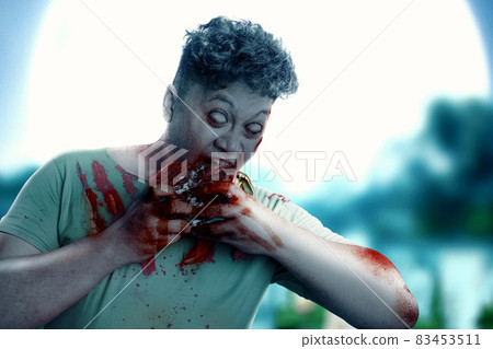 A scary zombie with blood and wound on his body eat the raw meat A scary zombie with blood and wound on his body eat the raw meat 83453511