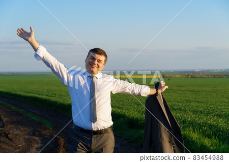 businessman walks along a country road, green field, freelance and business concept, green grass and blue sky as background 83454988