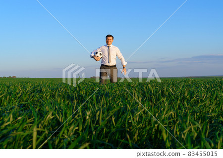 businessman poses with soccer ball in a green grass field - freelance, sport and business concept 83455015