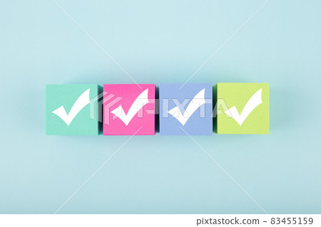 Four white checkmarks on multicolored cubes in a row against bright pastel blue background  83455159