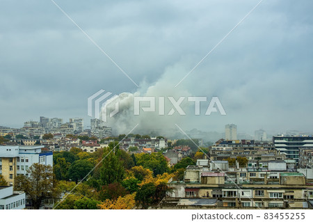 Huge cloud of gray smoke covers buildings during firefighting. City view with fire accident. Huge cloud of gray smoke covers buildings during firefighting. City view with fire accident. 83455255