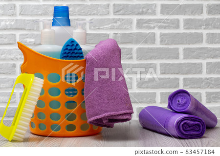 Bottles of dishwashing liquid, brush in a basket and garbage bags on gray background. Bottles of dishwashing liquid, brush in a basket and garbage bags on gray background. 83457184