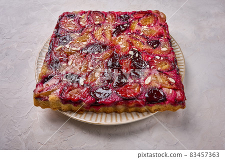 Close up traditional pie or tart with plums on plate on wooden background Close up traditional pie or tart with plums on plate on wooden background 83457363