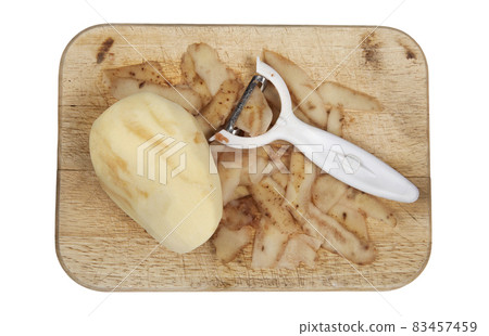 Raw potato peeled on a wooden chopping board with peeler cut out and isolated 83457459