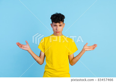 Cropped portrait of young boy in yellow T-shirt spreading hands isolated over blue background. Expression Cropped portrait of young boy in yellow T-shirt spreading hands isolated over blue background. Expression 83457466