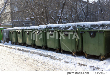 Green garbage containers on wheels covered with snow 83459626